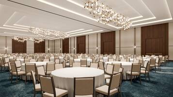 A large conference room with round tables and chairs, modern chandeliers, and wooden paneling.