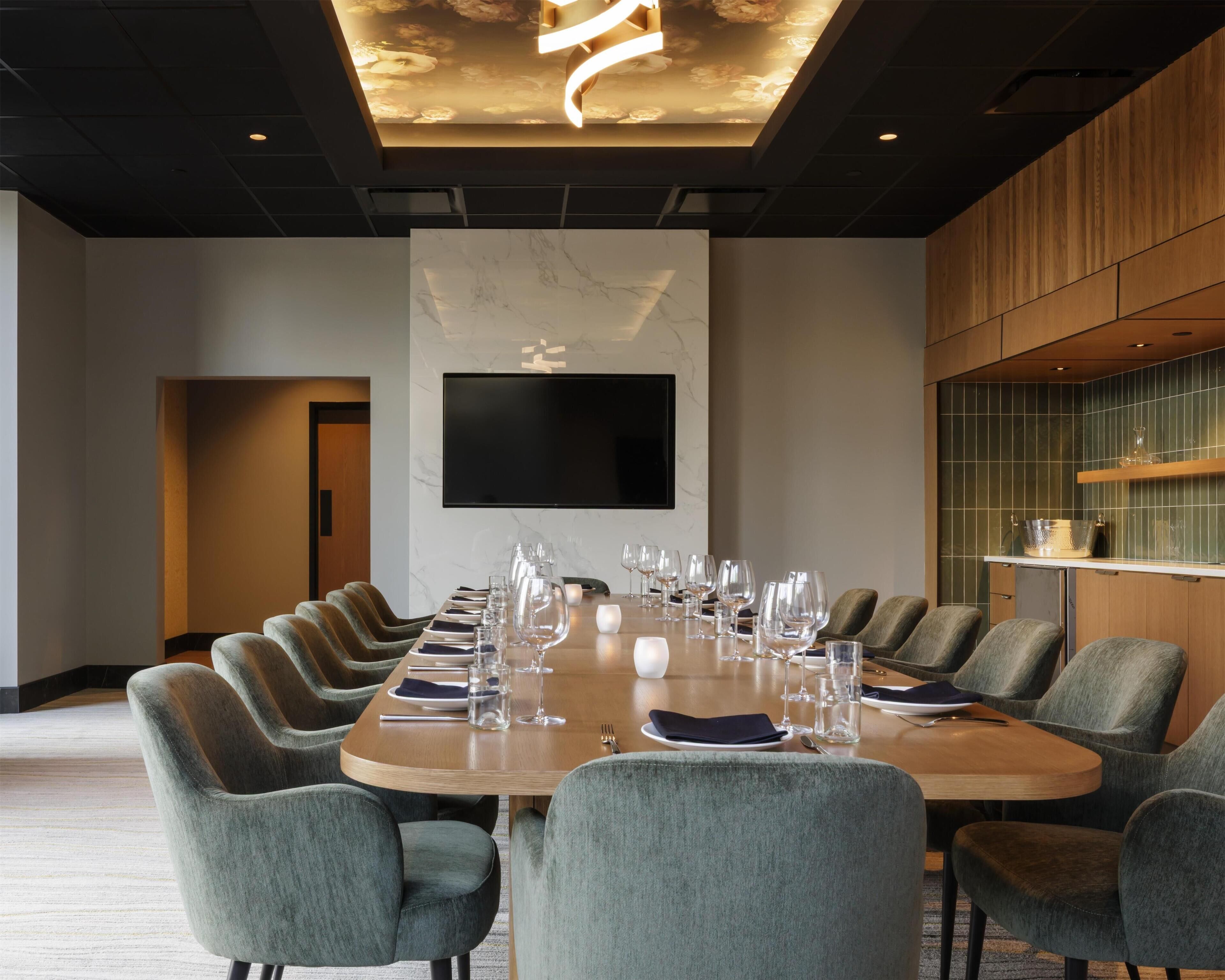 A conference room with a long table set for a meeting, surrounded by upholstered chairs.