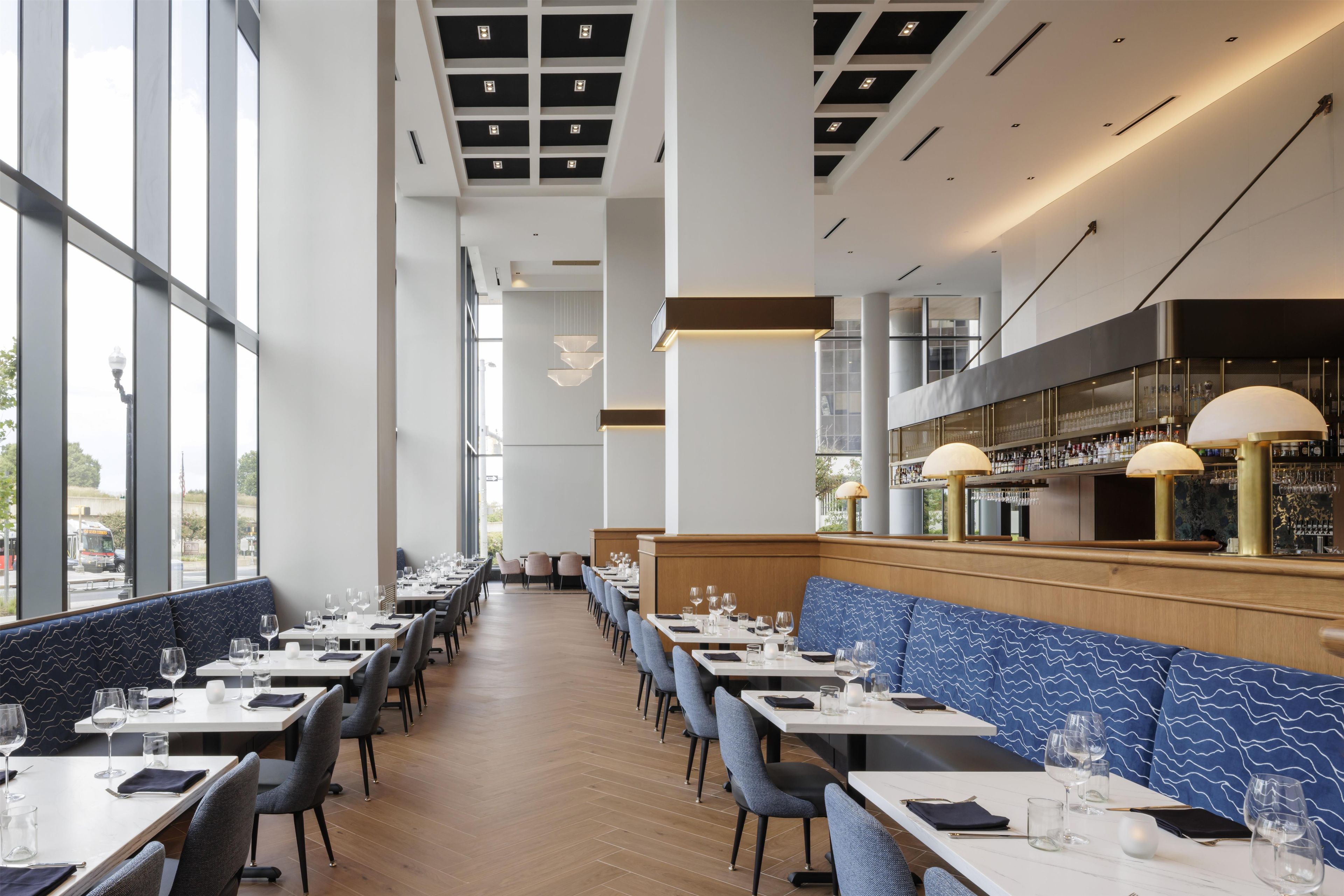 A restaurant interior with long tables, chairs, and a bar area.
