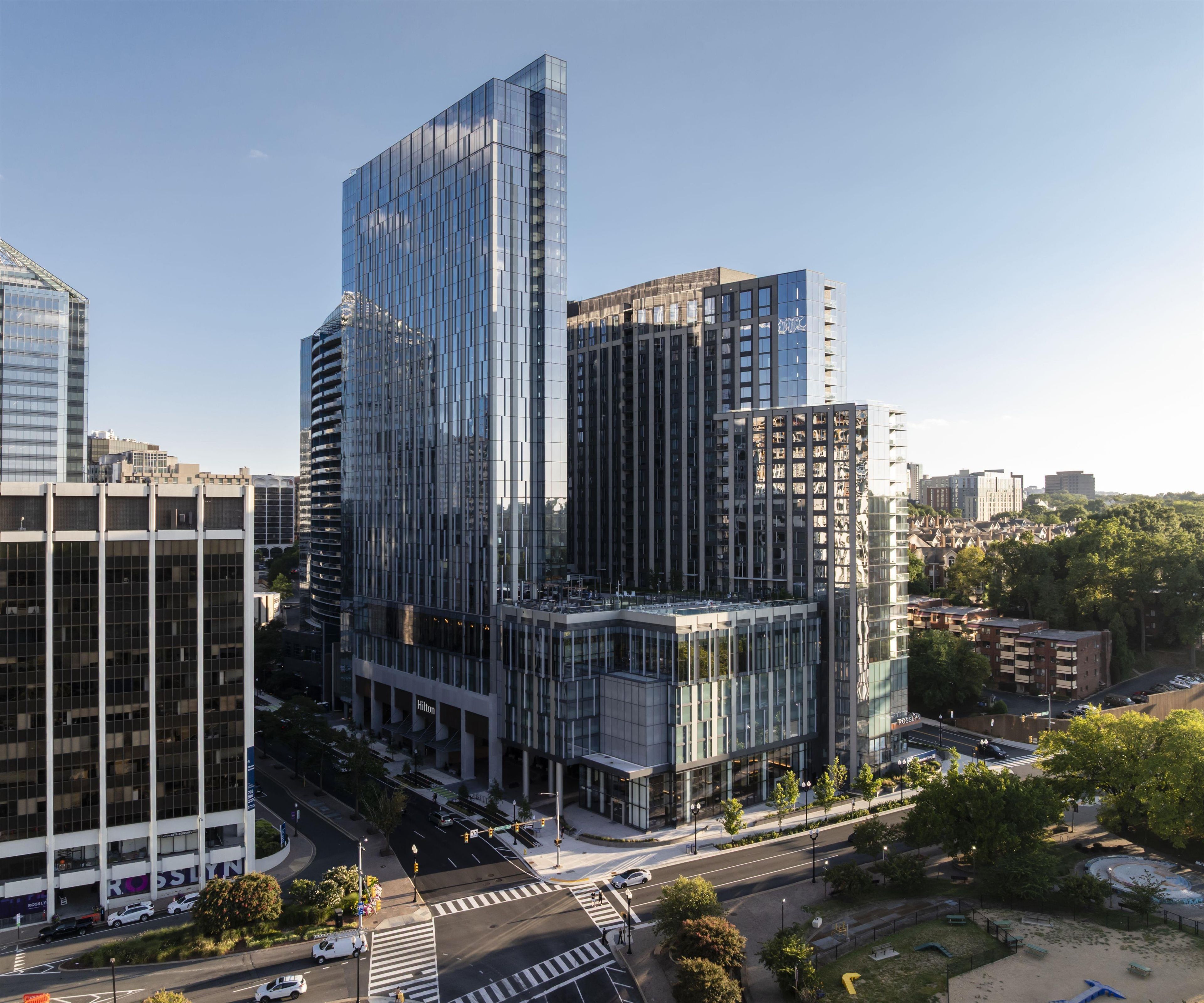 Um hotel moderno e imponente, com fachada de vidro, situado em área urbana com edifícios próximos.