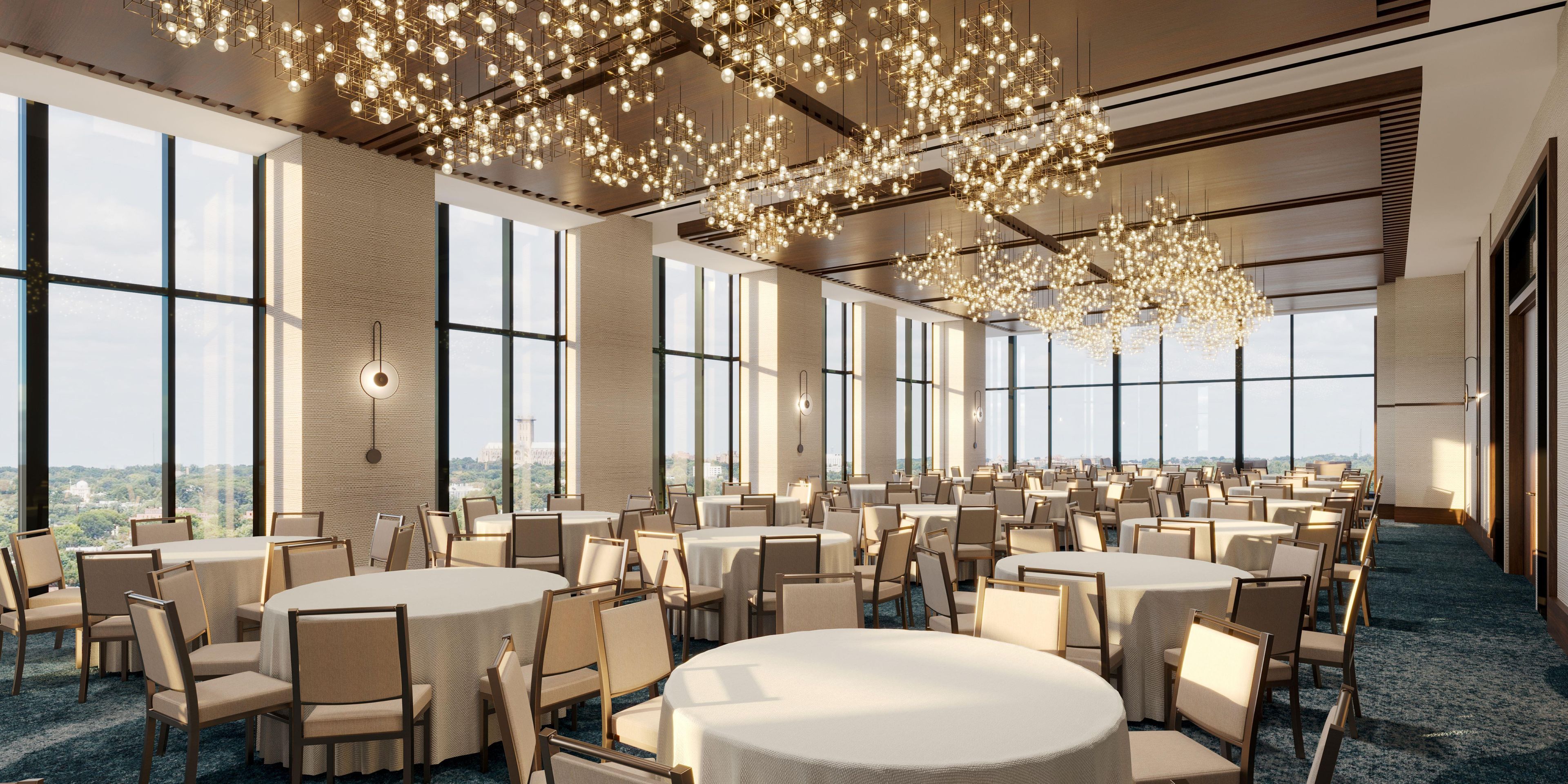 A spacious conference room with round tables and chairs, large windows offering a city view, and a modern chandelier.