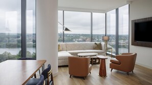 A spacious living room with a large window, a sofa, two armchairs, a coffee table, and a flat-screen TV mounted on the wall. - Hilton Arlington Rosslyn The Key (Arlington)