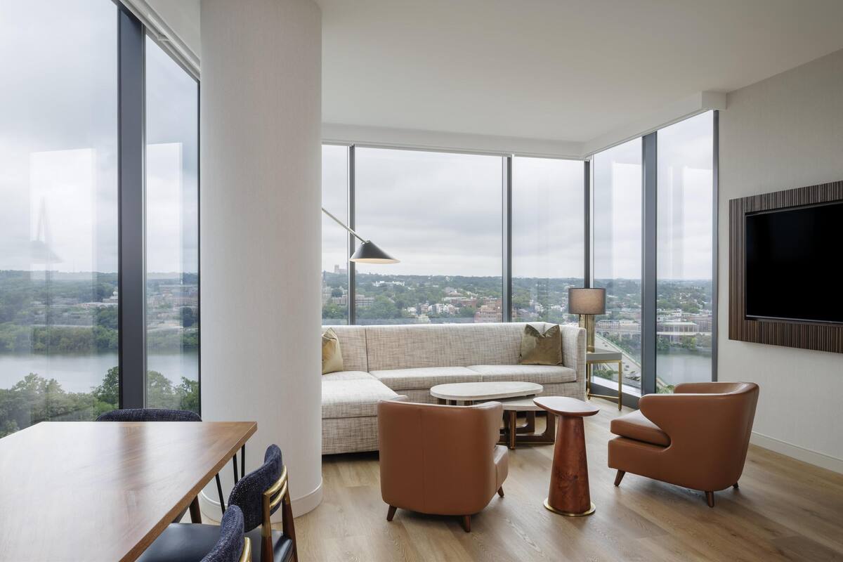 Un salon spacieux doté d’une grande fenêtre, d’un canapé, de deux fauteuils, d’une table basse et d’un téléviseur à écran plat fixé au mur.