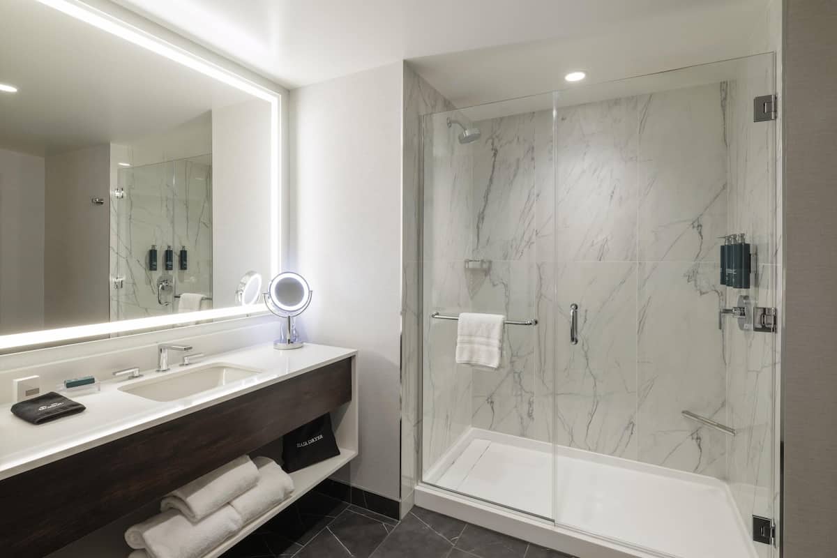 Une salle de bain moderne avec un grand miroir, un meuble-lavabo en bois foncé, une douche à parois de verre et un lavabo blanc.