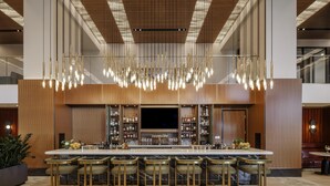 A modern bar area with a long counter, multiple stools, and a large chandelier. - Hilton Arlington Rosslyn The Key (Arlington)