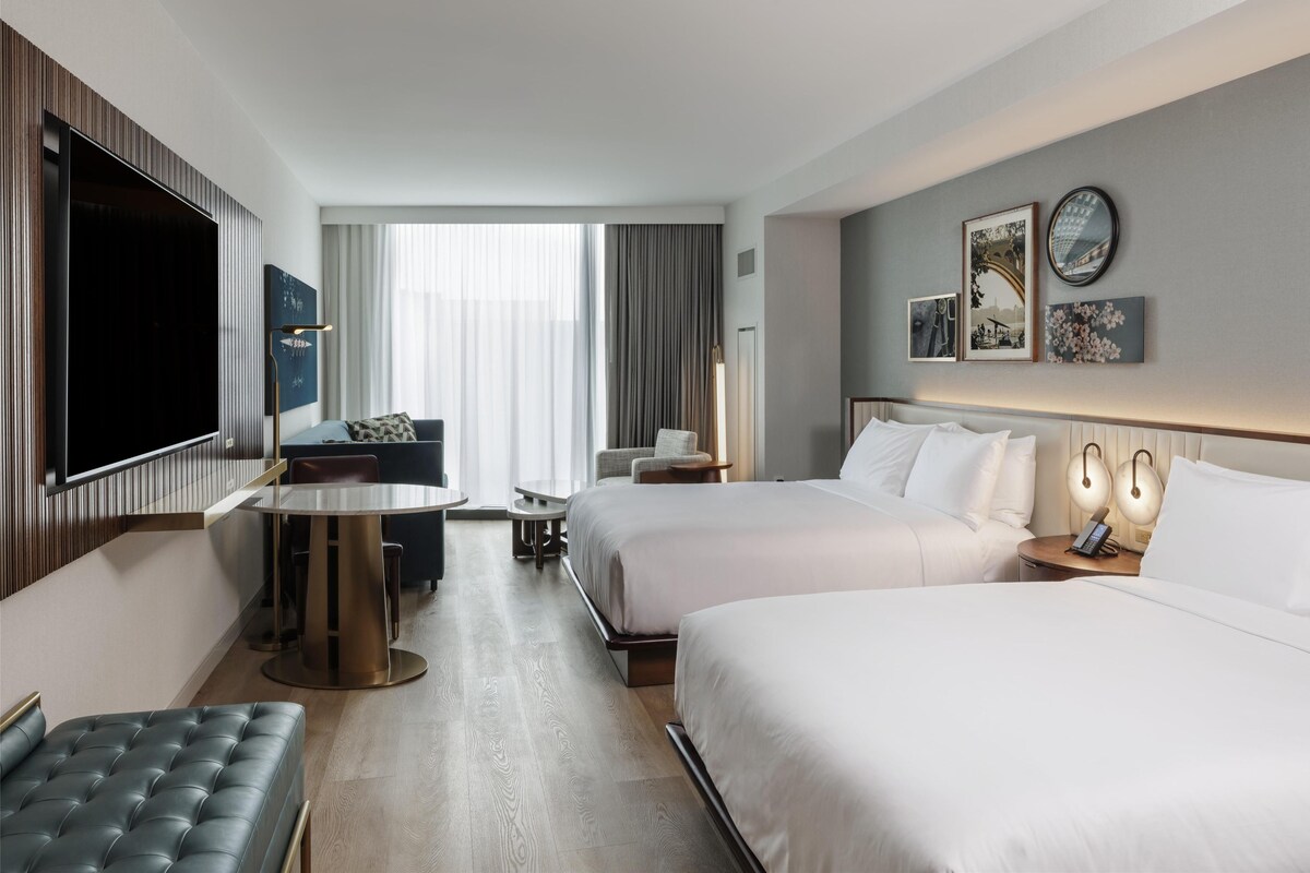 A hotel room with two beds, a flat-screen TV, a dining table, and a seating area.