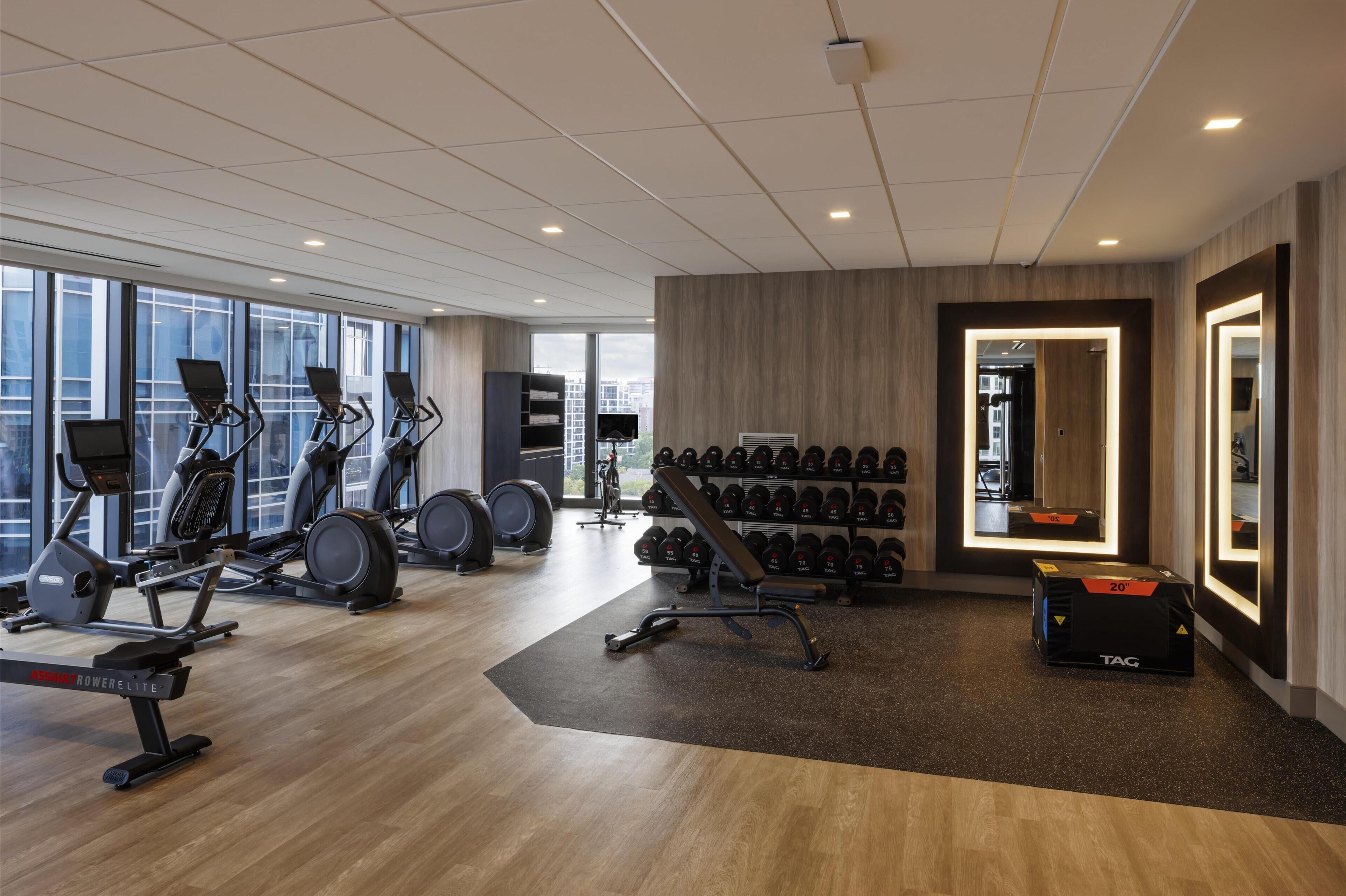 Uma academia moderna com equipamentos de cardio, suportes para pesos e um espelho.