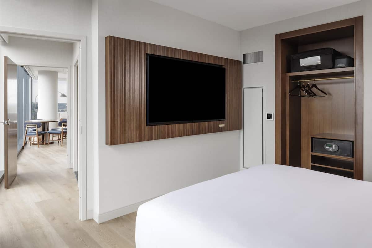 Une chambre d’hôtel moderne dotée d’un grand lit, d’un téléviseur fixé au mur et d’un dressing avec un four à micro-ondes.