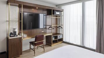 Habitación de hotel con una cama grande, un escritorio con silla, televisor y armario con estantes y zona para colgar ropa.