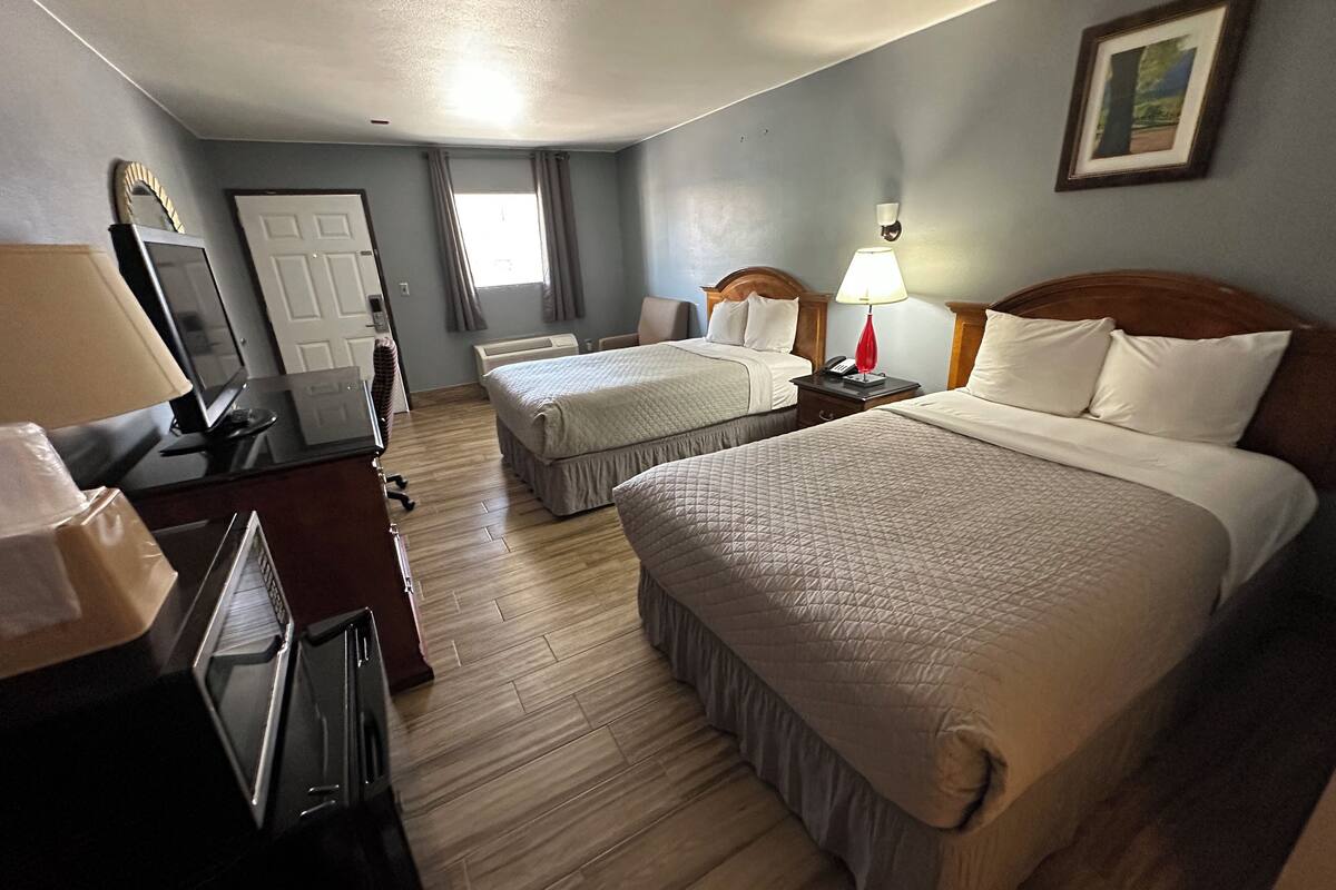 A hotel room with two beds, a desk with a computer, a TV, and a lamp.