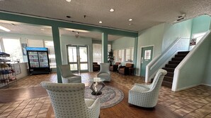 Un hall con suelo de baldosas, zona de estar con sillones estampados, una mesa de centro de cristal y un refrigerador lleno de bebidas.