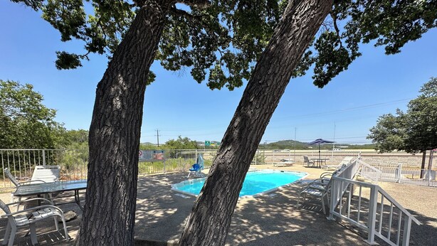 Una piscina rodeada de árboles, con una zona delimitada por una cerca y una banca.