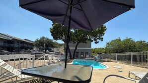 Zona de piscina con sillas de descanso y una mesa bajo una sombrilla.