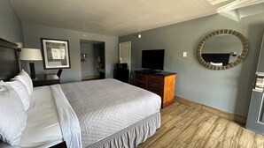 Habitación de hotel con cama, televisor, cómoda, espejo y un cuadro en la pared.