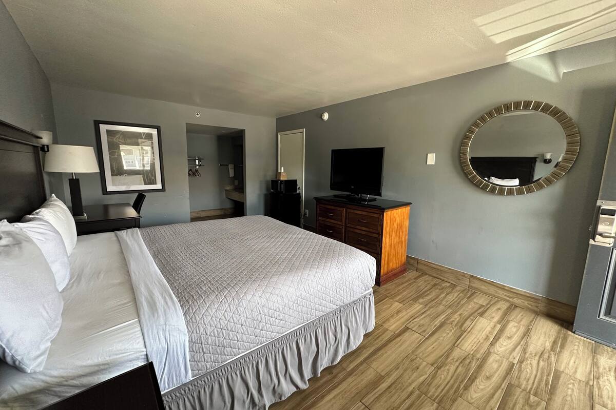 A hotel room with a bed, a TV, a dresser, a mirror, and a framed picture on the wall.