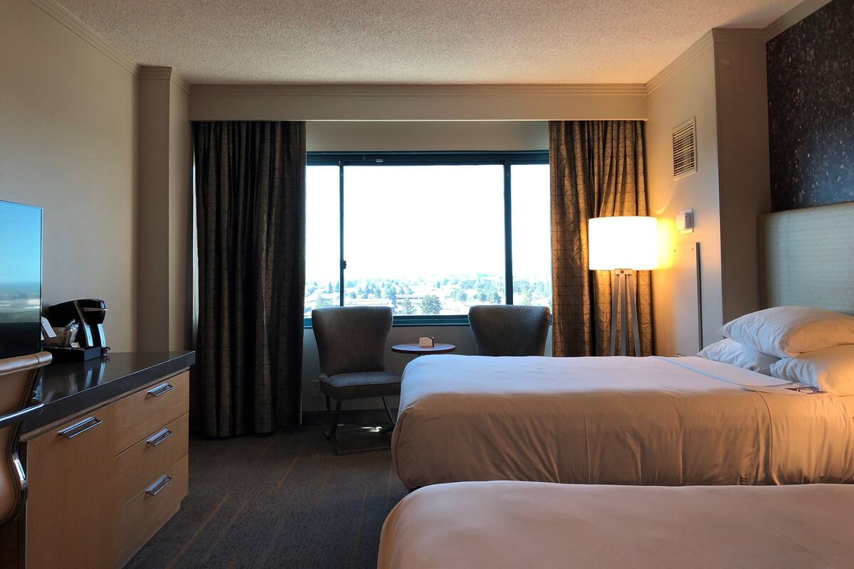 A hotel room with two beds, a desk, a chair, a TV, and a window with curtains.
