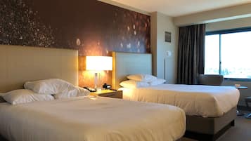 Habitación de hotel con dos camas, una mesita de noche con lámpara, una silla y una ventana con cortinas.