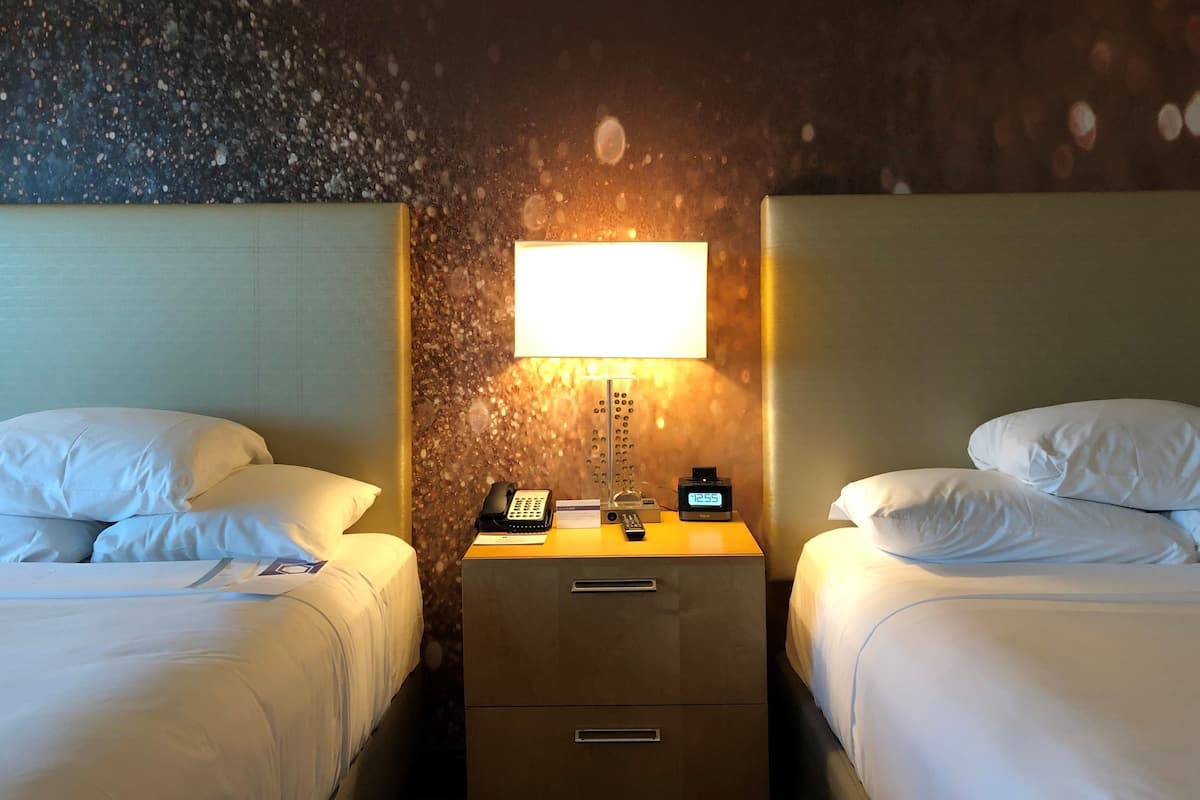 A hotel room with two beds, a nightstand with a lamp, a clock, and a telephone.