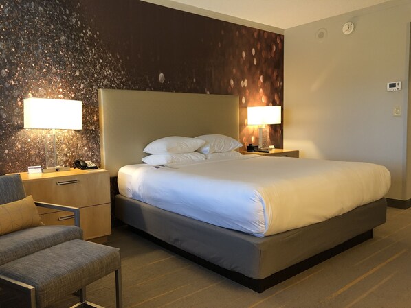 A hotel room with a large bed, two bedside lamps, a nightstand, a chair, and a textured wall.