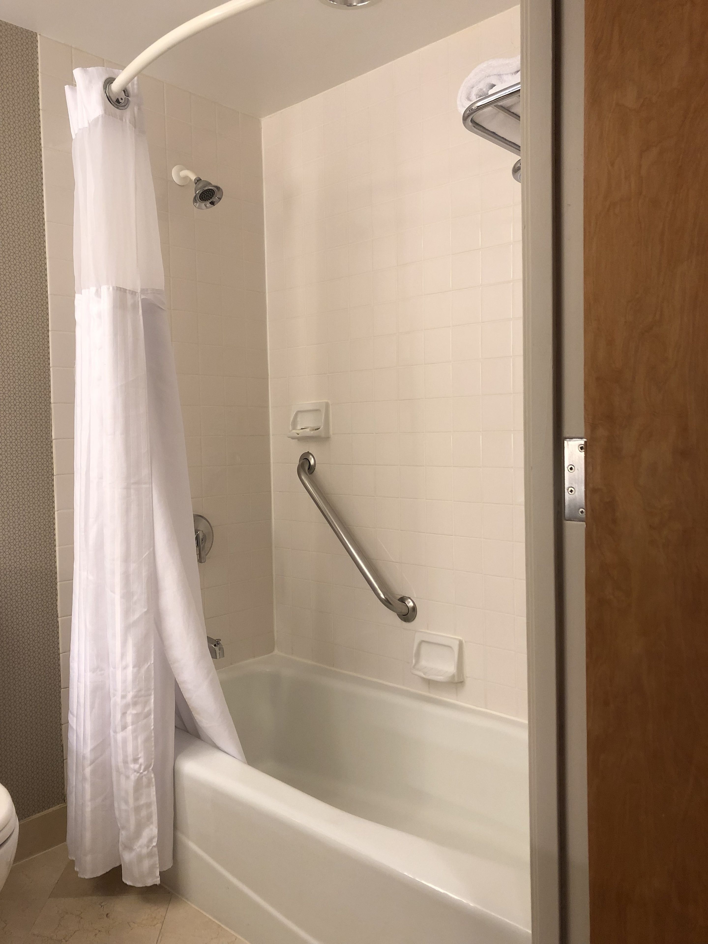 A shower with a white curtain, a grab bar, and a handheld showerhead.