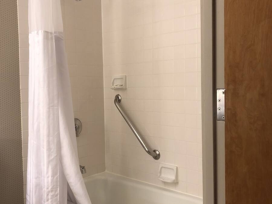 A shower with a white curtain, a grab bar, and a handheld showerhead.