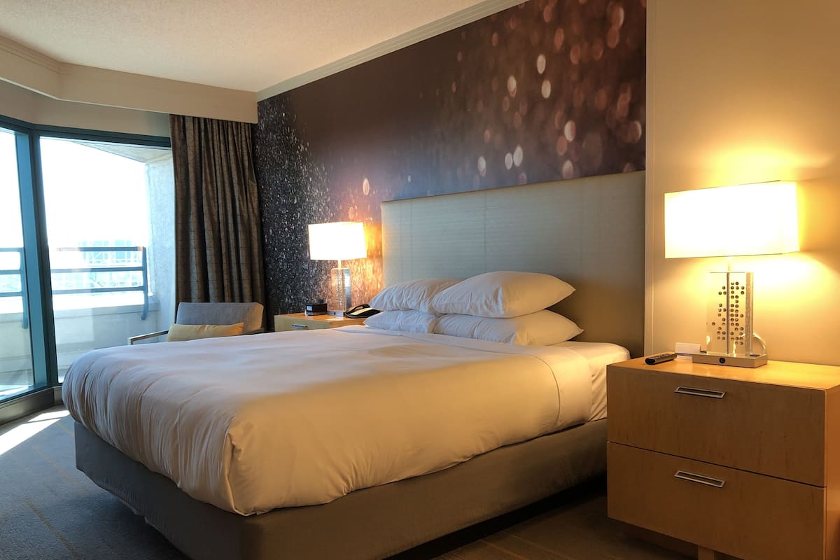 A hotel room with a large bed, two bedside tables, a desk with a lamp, and a view of the outdoors.