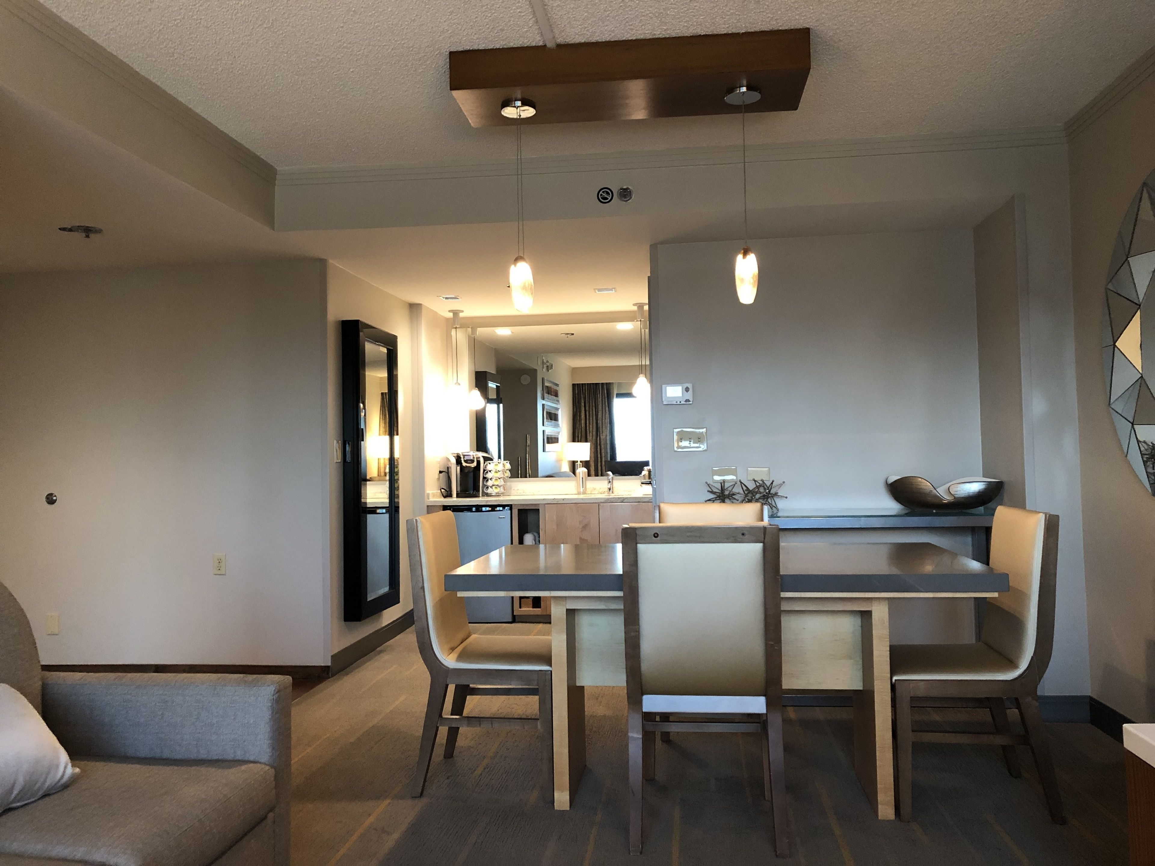 A modern dining area with a rectangular table and four chairs, a sofa, and a kitchen in the background.