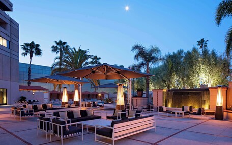 An outdoor seating area with tables and chairs, umbrellas, and a pool in the background.