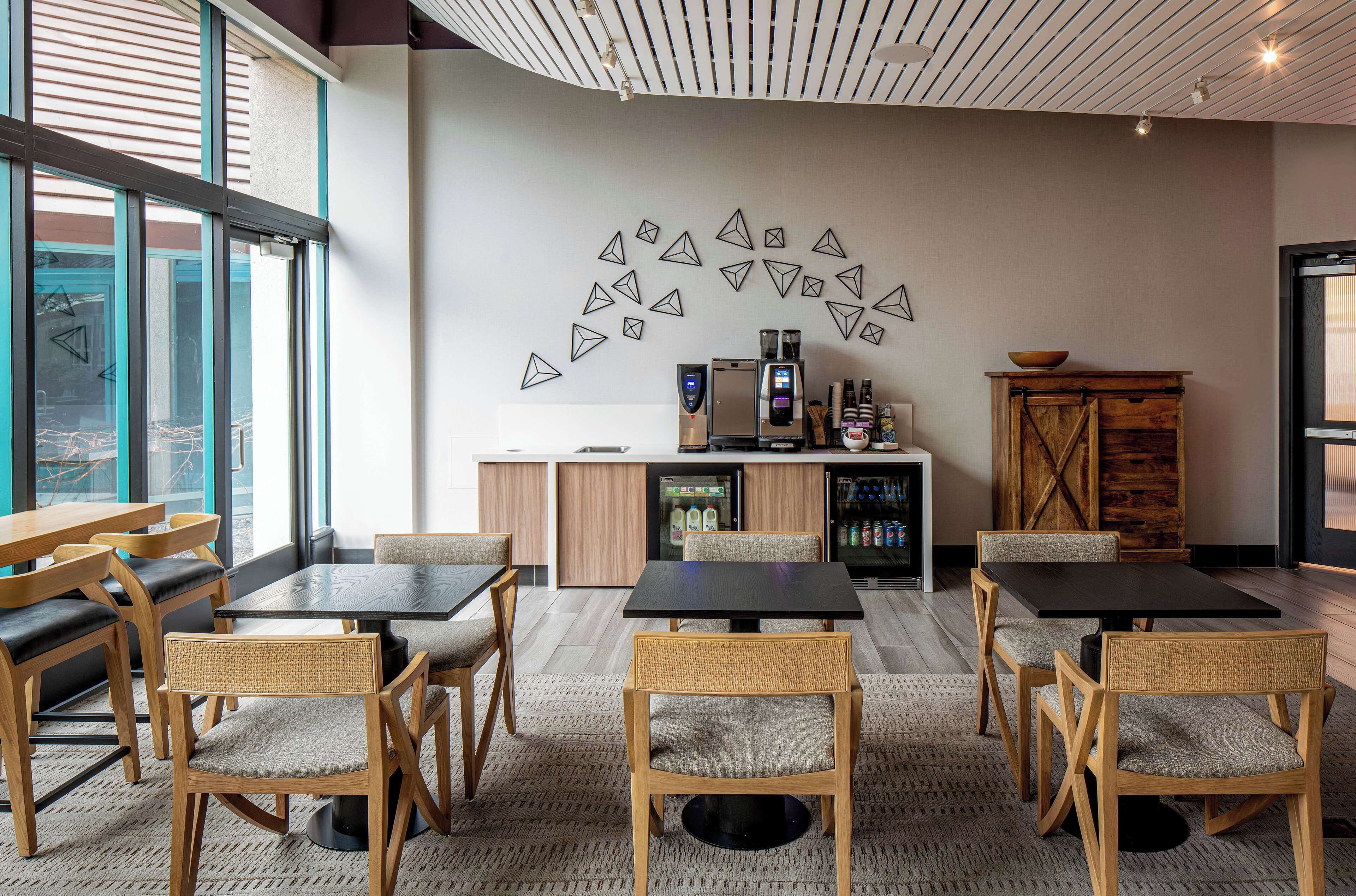 A modern dining area with wooden tables and chairs, a refrigerator, and a decorative wall with geometric shapes.