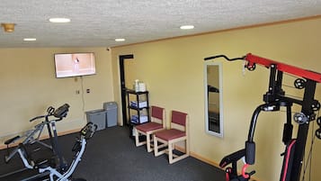 Une salle de sport équipée de matériel d’exercice, d’un téléviseur et de coins salon.