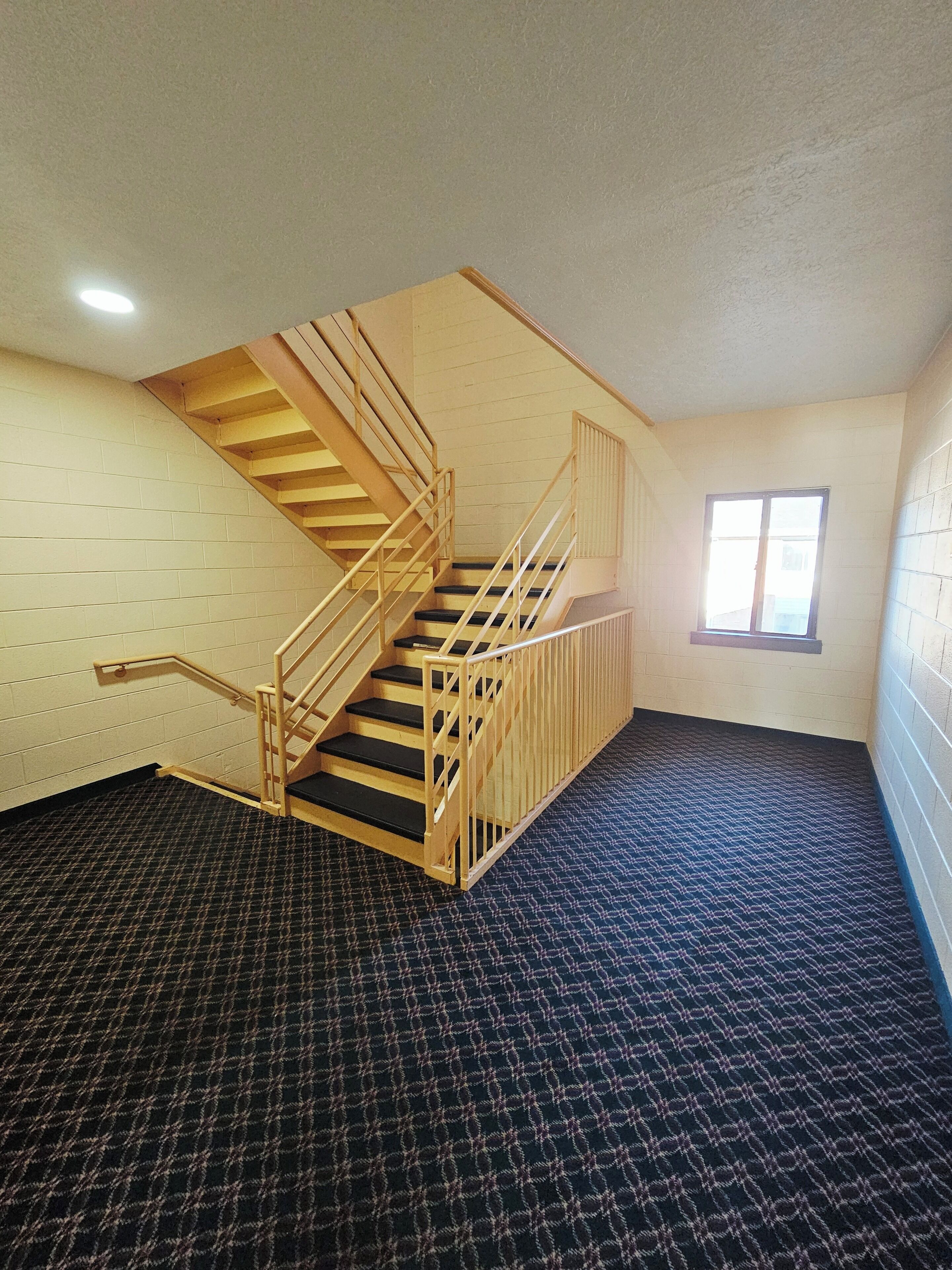 A room with a wooden staircase, a window, and a patterned carpet.