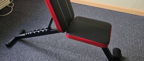 Um banco preto e vermelho com um logotipo, colocado sobre um piso coberto de carpete perto de uma tomada.