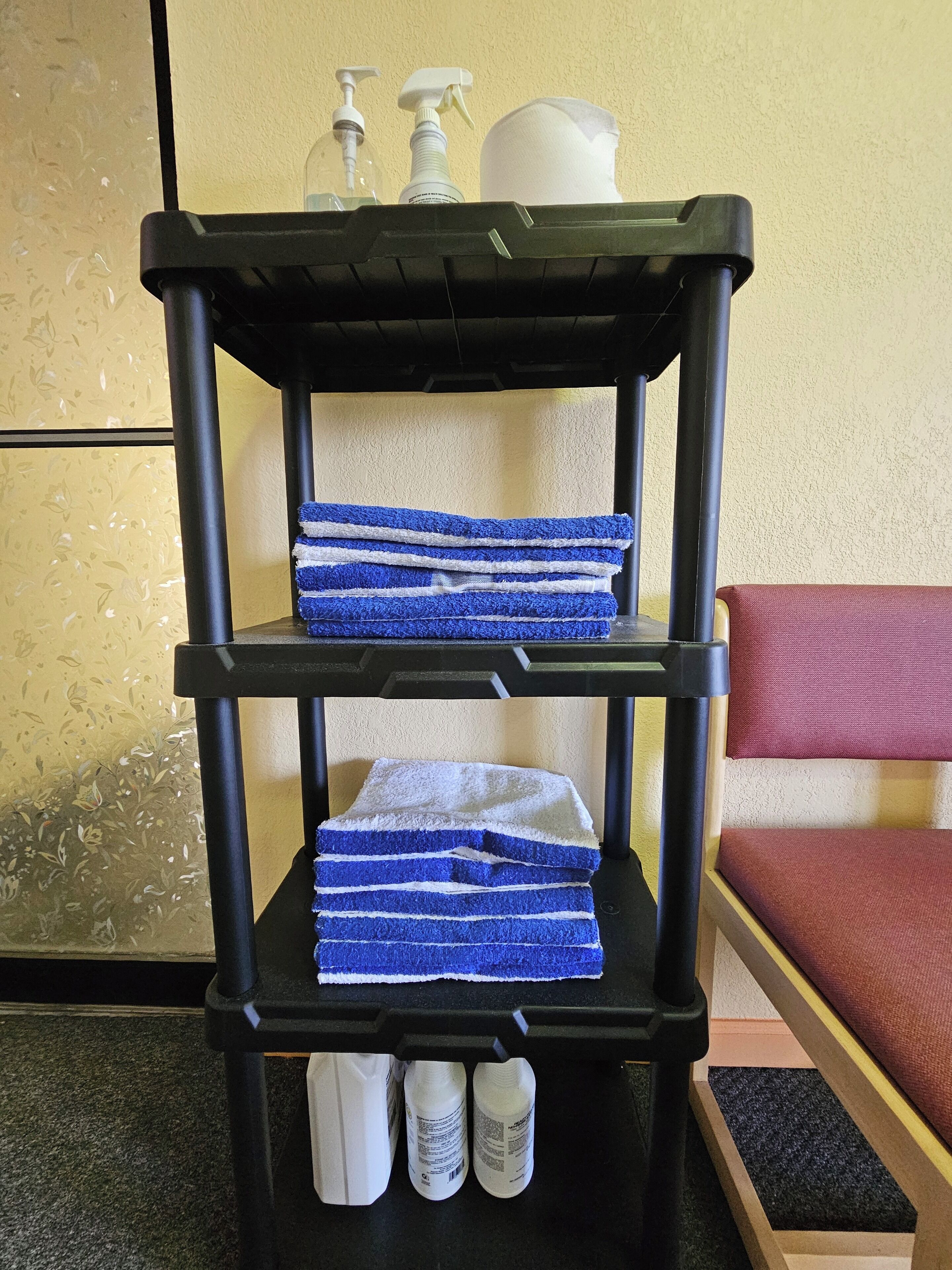 A black shelf with blue and white striped towels stacked on it, a white pitcher, and two bottles of hand soap.