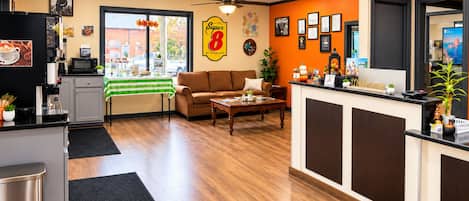 A hotel lobby with a reception desk, a sofa, a coffee station, and a view of the street.