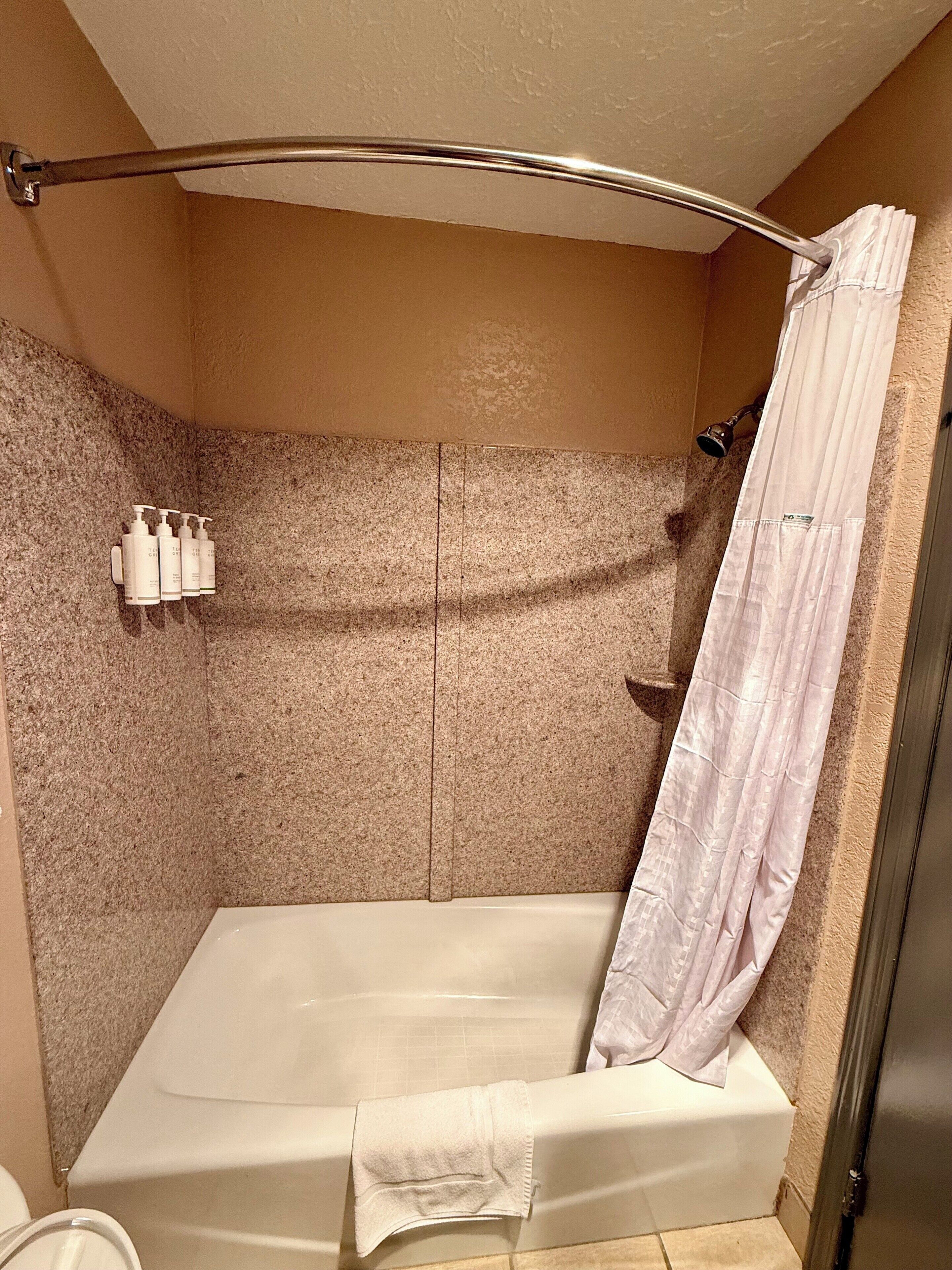 A bathroom with a shower, a bathtub, and a towel rack with bottles.