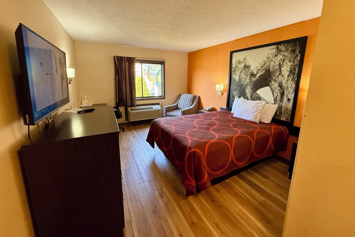 A hotel room with a bed, a desk, a chair, a TV, and a window with curtains.