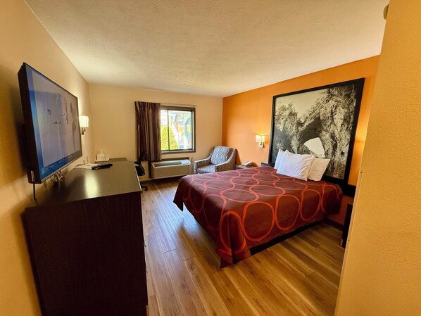 Habitación de hotel con cama, escritorio, silla, televisión y ventana con cortinas.