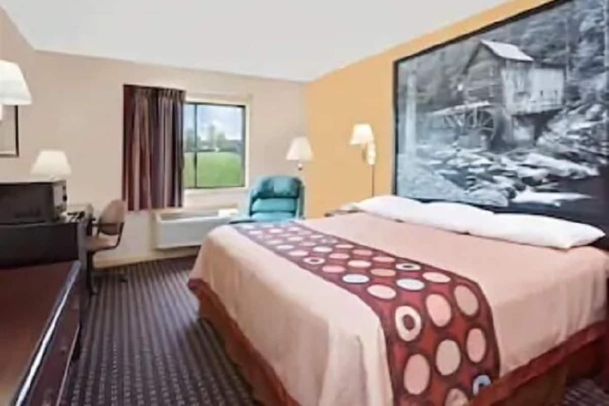A hotel room with a bed, a desk, a chair, a window, and a painting on the wall.
