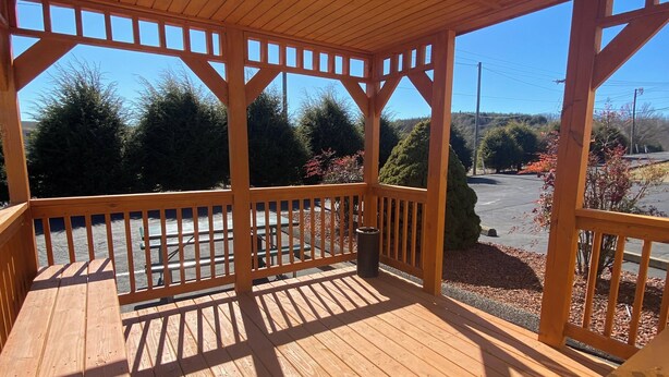 A wooden gazebo with a clear view of the surrounding landscape, including trees and a parking area.