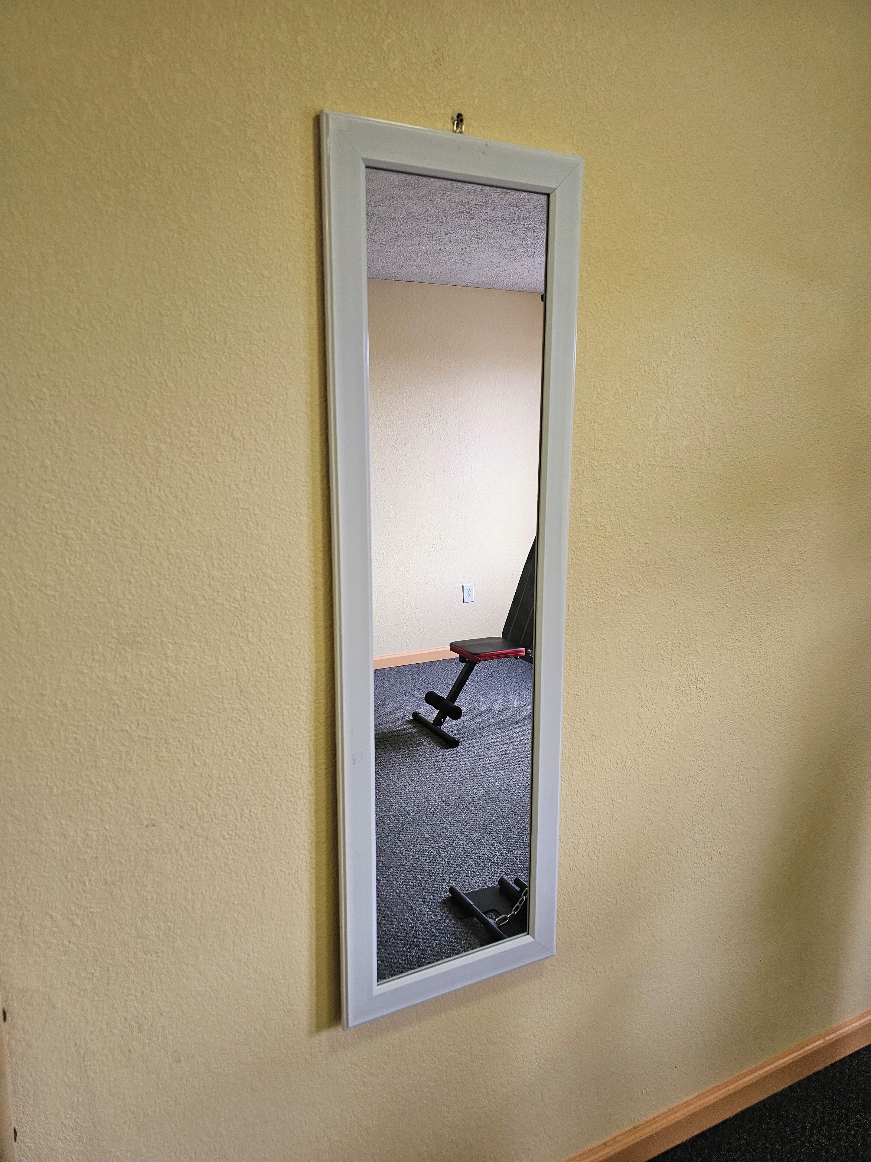 A mirror with a white frame mounted on a beige wall.