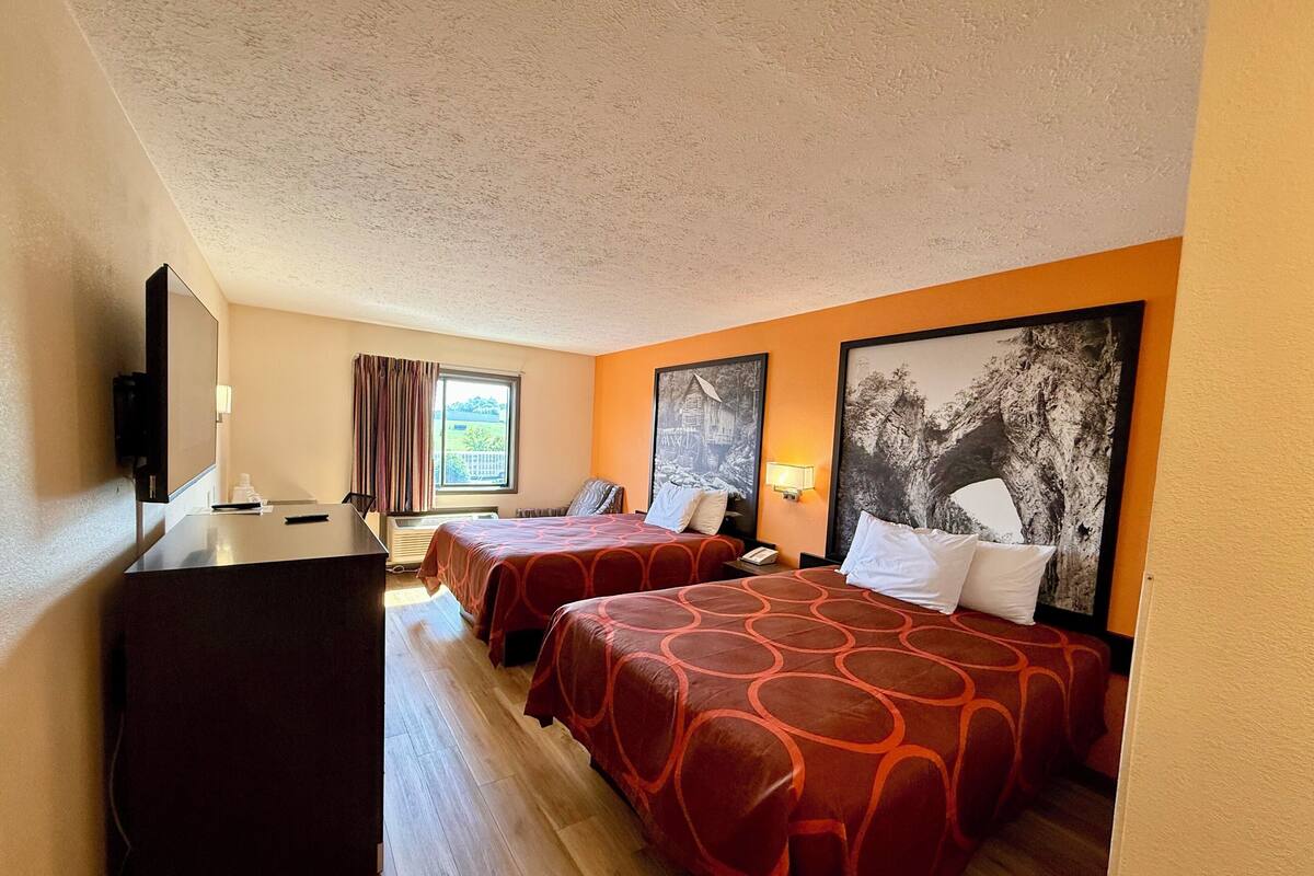 A hotel room with two beds, a desk, a TV, and a window with curtains.