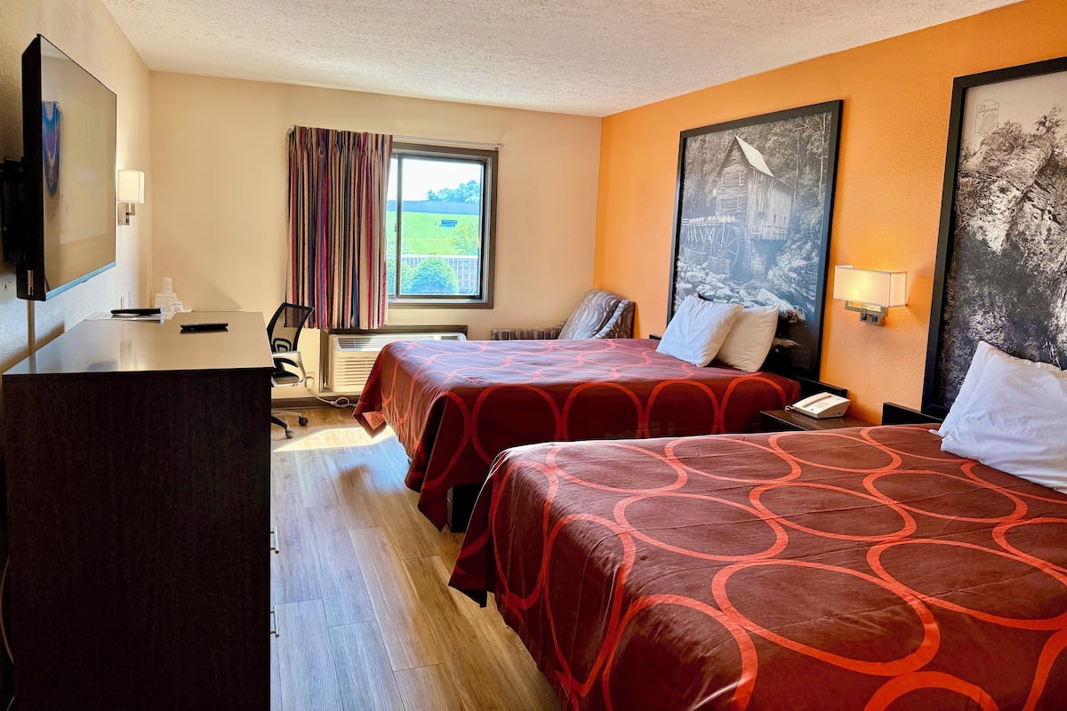 A hotel room with two beds, a desk with a computer, a TV, and a window with curtains.