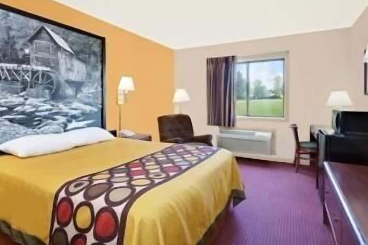 A hotel room with a bed, a desk, a chair, a window, and a painting on the wall.