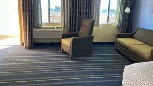 A hotel room with a striped carpet, a sofa, a chair, and a window with curtains.