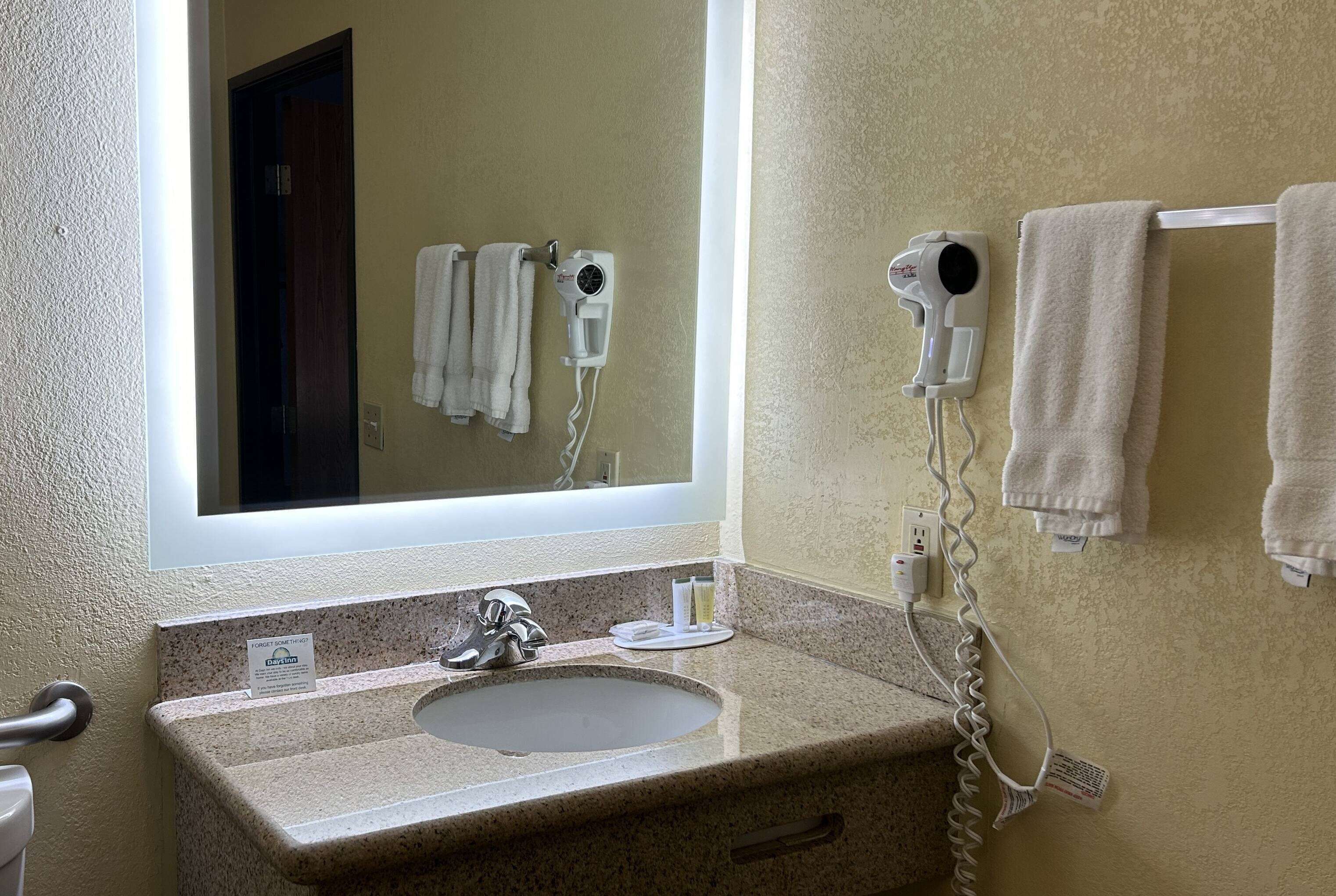 Un baño con lavamanos de granito, un espejo, dos secadores de pelo montados en la pared y un perchero con toallas.