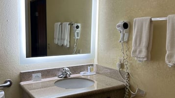Un baño con lavamanos de granito, un espejo, dos secadores de pelo montados en la pared y un perchero con toallas.