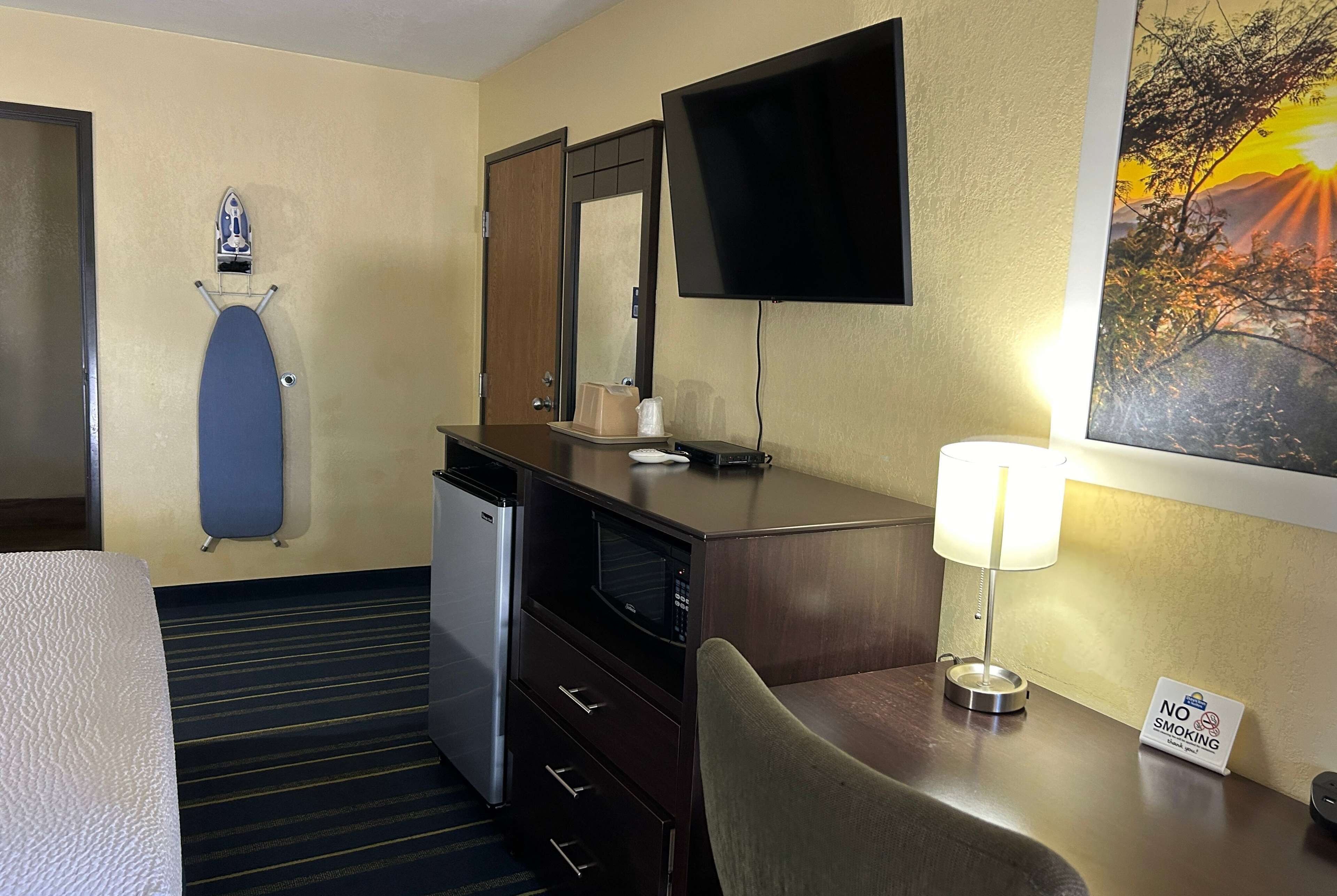 Habitació d'hotel amb un llit, un escriptori amb una làmpada, microones, un refrigerador petit, televisió penjada a la paret, un quadre del capvespre i un senyalitzador de 'No Fumar'.