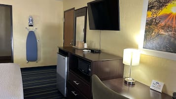 Habitación de hotel con cama, escritorio con lámpara, microondas, refrigerador pequeño, televisor montado en la pared, pintura de un atardecer y un cartel de 'No Smoking'.