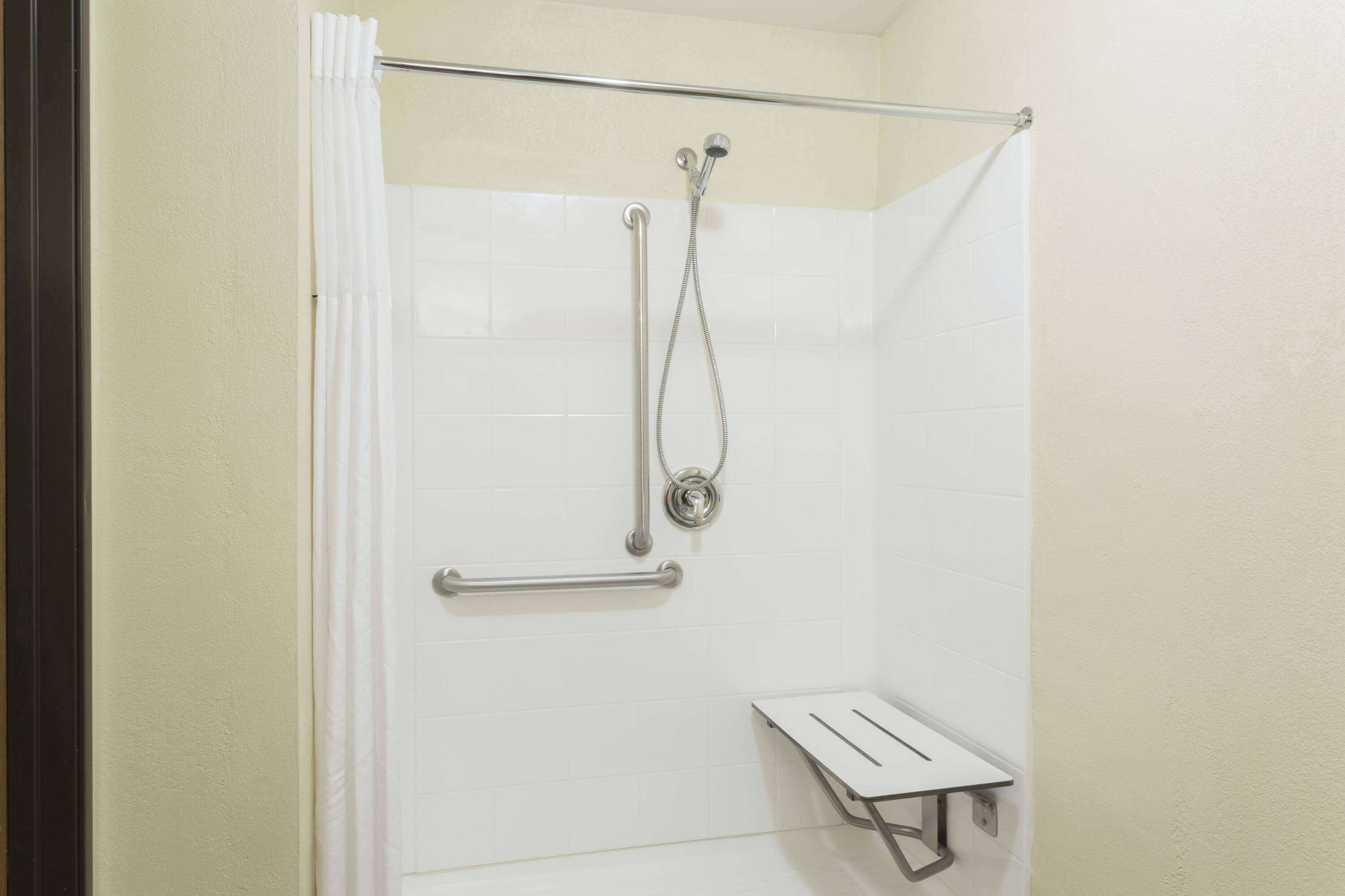 A shower area with a grab bar, a showerhead, and a small shelf.