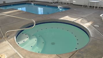 A swimming pool with a hot tub, surrounded by lounge chairs and a sunlit patio area.
